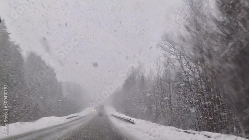 The car is driving along the highway through snow and blizzard. Video through the windshield on a winter storm.