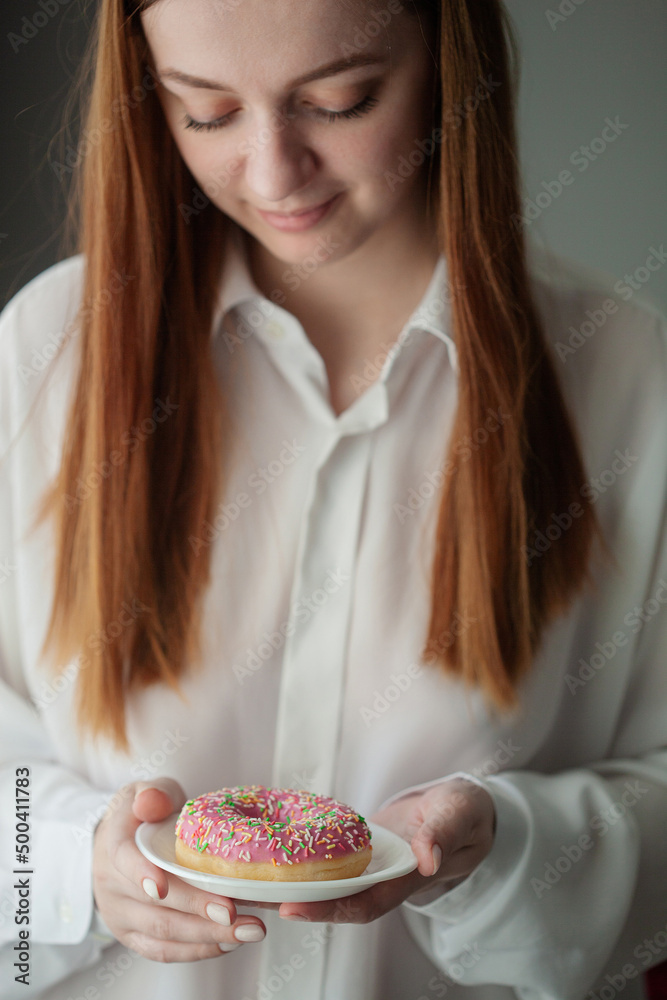a girl in a white shirt holds a saucer with a fresh fragrant tasty donut of strawberry flavor in her hands a girl in a white shirt holds a saucer with a fresh fragrant tasty donut of strawberry flavor in her hands