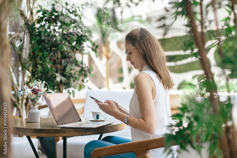 young woman using a smartphone and a laptop sitting at a table in a cafe. young woman using a smartphone and a laptop sitting at a table in a cafe.