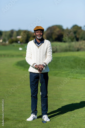 middle aged african american man standing with golf club on green field.