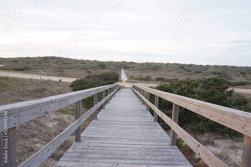 Weathered Boardwalk with Railing Through Sand and Grassy Dune