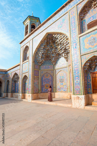 Woman in traditional abaya standing in the Nasir al-Mulk Mosque (Pink Mosque) reflected in pool in the middle of courtyard in Shiraz, Iran - Also famous as Pink Mosque