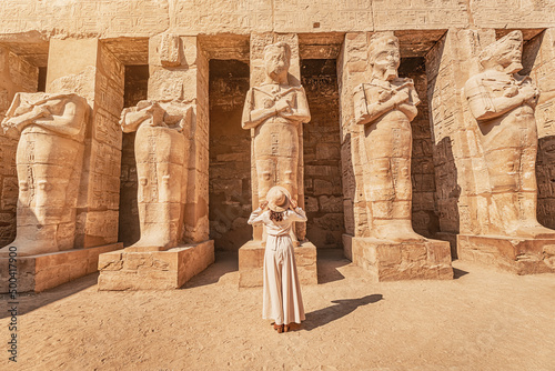 Obraz na płótnie A happy tourist girl in a dress is interested in Egyptology and archaeology and gets a travel experience at the Karnak Temple in Luxor. w salonie
