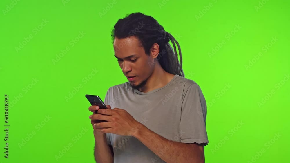 Young excited African American man student quickly typing text on phone trying to send SMS message on time and rejoices after completion stands on green studio background. Mobile technology, chatting Young excited African American man student quickly typing text on phone trying to send SMS message on time and rejoices after completion stands on green studio background. Mobile technology, chatting
