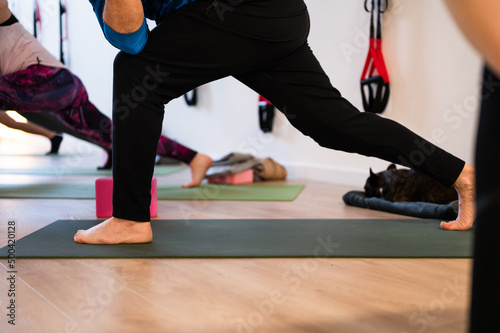 Legs and feet of group of people with focus on man practicing yoga in studio. Active lifestyle people stretching on exercise mats. Unrecognizable persons working out.