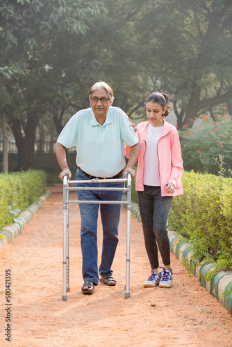 Canvas Print Senior citizen man use a walker in the park with granddaughter.