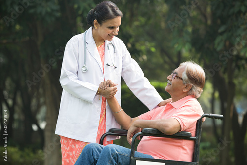 Female physical therapist discussing with senior man in wheelchair at park