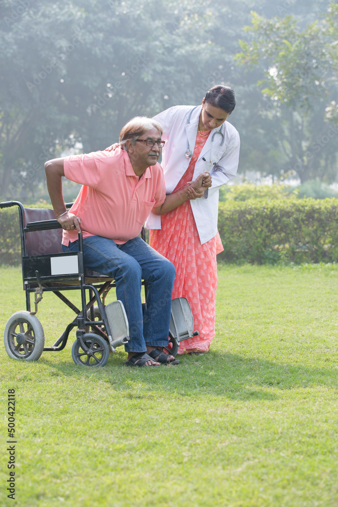 Female doctor discussing with senior man in wheelchair at park Female doctor discussing with senior man in wheelchair at park