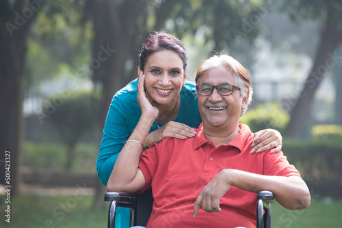 Photography Female physical therapist discussing with senior man in wheelchair at park