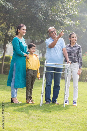 Happy family admiring view at park with old man using mobility walker 