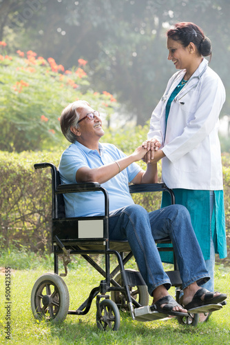 Female doctor discussing with senior man in wheelchair at park