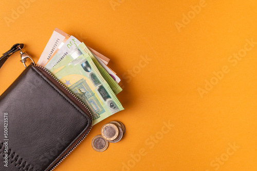 euro banknotes and coins in a black portmanteau on an orange background top view with space for text