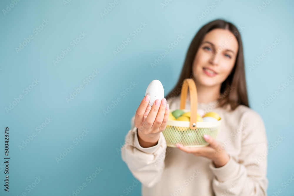 Cute brunette woman holds painted Easter eggs in basket in her hands, Easter, in the studio on a blue background. Cute brunette woman holds painted Easter eggs in basket in her hands, Easter, in the studio on a blue background.