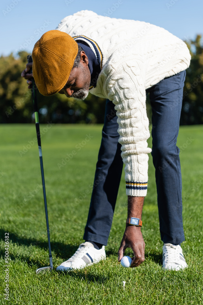 Obraz premium bearded african american man placing ball on golf tee.