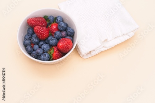mixed fresh organic berries in a bowl with white napkin on a beige table