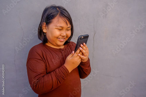 Portrait of young fun smart happy little asian girl holding smart phone isolated on wall background. Education for elementary kindergarten.
