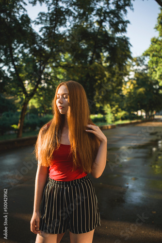 Young beautiful red-haired long-haired woman in a summer pink dress walks through the streets of a summer city.