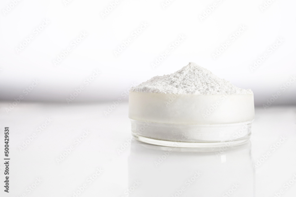 A container with zinc oxide on a white blurred background with reflection. Chemistry, health care, cosmetics production. - obrazy, fototapety, plakaty 