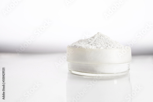 A container with zinc oxide on a white blurred background with reflection. Chemistry, health care, cosmetics production. photo