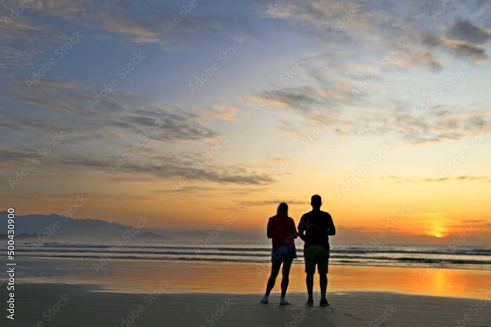 Red sky, rising sun, lots of light in the ocean waters. Magnificent marine sunset scene. Couple watching sunrise on the beach in the morning. Vibrant colors of the sun, reflections in the water 