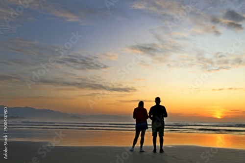 Red sky, rising sun, lots of light in the ocean waters. Magnificent marine sunset scene. Couple watching sunrise on the beach in the morning. Vibrant colors of the sun, reflections in the water  © valdecilima