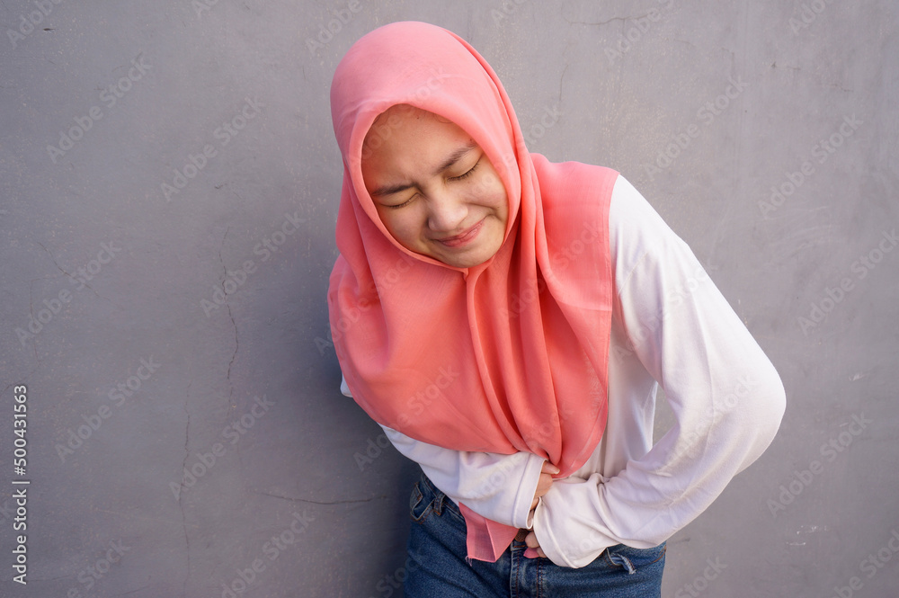 Cute Asian muslim woman in pain with both hands holding stomach when stomachache Cute Asian muslim woman in pain with both hands holding stomach when stomachache