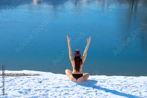 Winter hardy woman back view body with raised hands up on snow - white bank of the blue lake background copy space photo