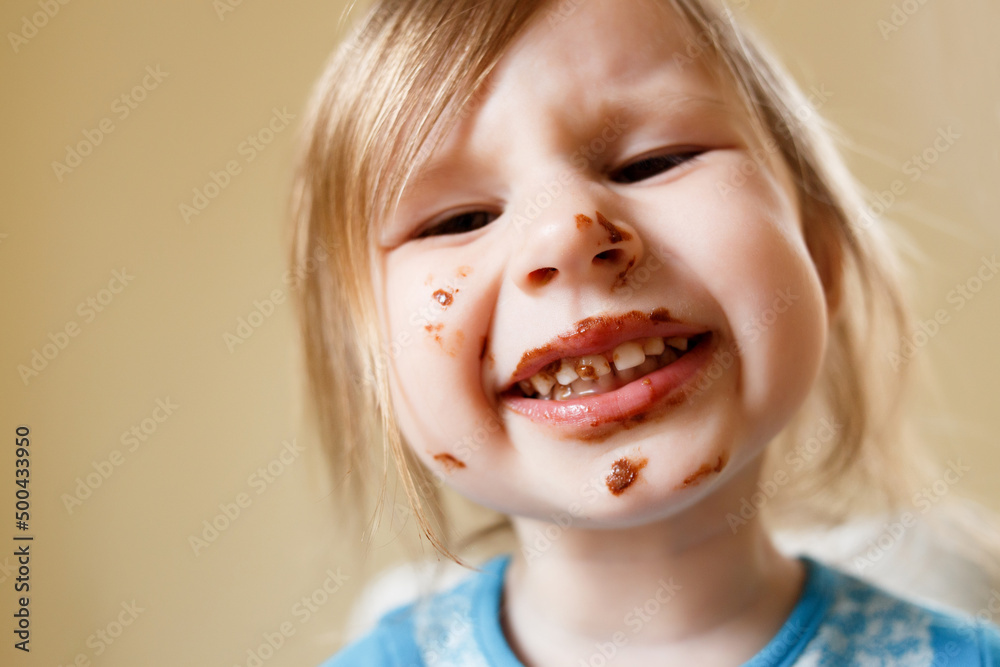 The little girl got covered in chocolate. Face close-up. Dissatisfied face, teeth hurt.