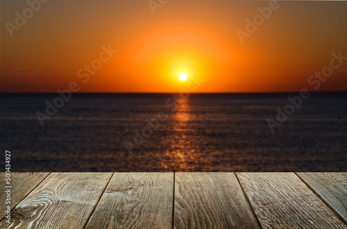 An empty brown wooden table. Blurred background with sunset on the sea. © mitand73