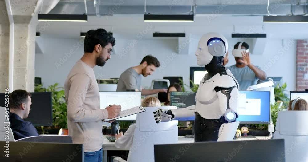 Man talking with robot in office. Male developer checking work of machine by document. Coworking space. Humanoid moving and executing instructions and orders. Conversation with AI. Man talking with robot in office. Male developer checking work of machine by document. Coworking space. Humanoid moving and executing instructions and orders. Conversation with AI.