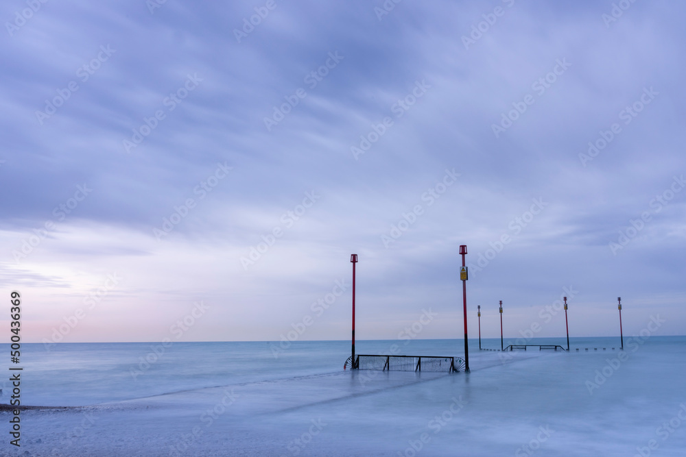Discharge pipes and marker posts in a calm sea at dawn
