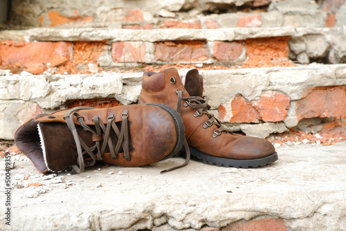 A pair of old worn brown leather shoes with laces on an old brick porch.The concept of proper care for leather shoes.The timing of the return of shoes to the store.