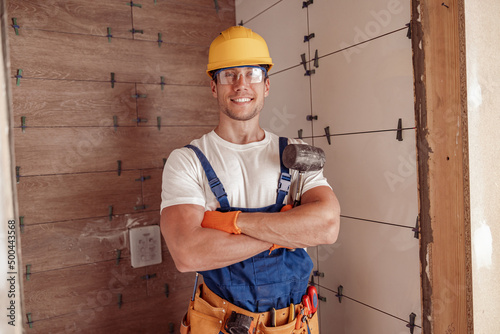 Cheerful male builder standing by the wall with ceramic tile photo