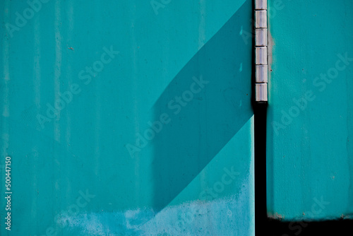 Abstract of turquoise, exterior metal door with chrome hinge © Annee