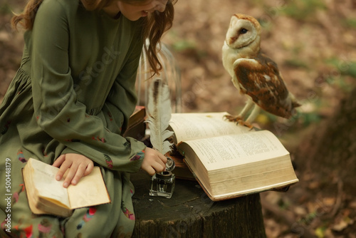 The girl writes with a pen. Near sits an owl on an open book. Forest background.