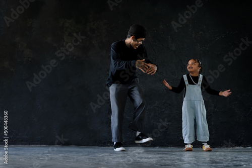 Cute little African kid boy and cool young Asian man teacher with tattoo are practice hip hop or freestyle dancing on cement floor on black background. Child education on free time