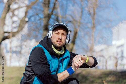 Athlete focused on running training for marathon, preparing for morning run, motivational music in headphones, athletic man turns on watch app monitoring heart rate, route.