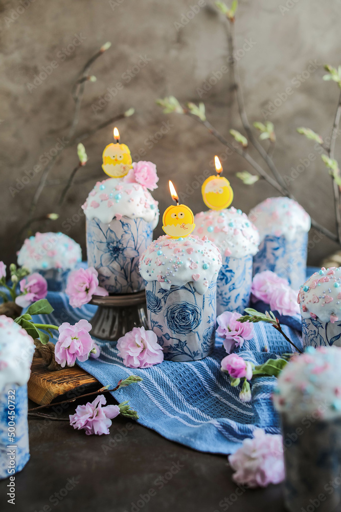 Fototapeta premium Beautiful Easter cakes in glaze and confectionery sprinkles and candles. Easter traditional treats and festive table decor