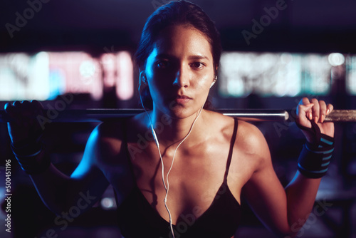  young and strong latin woman lifting a weight in the gym while listening to music with headphones
