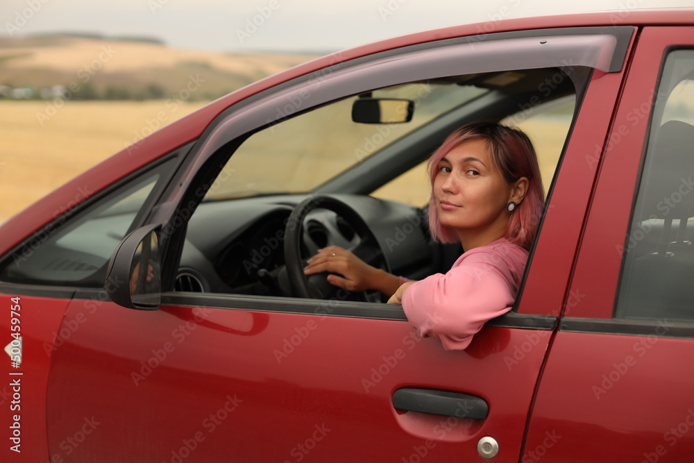 A young woman with pink hair is driving her car