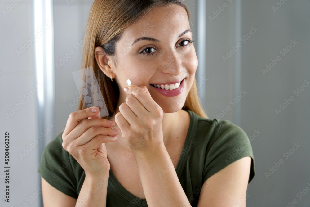 Close-up of smiling girl applying acne treatment anti-pickel patch on a pimple in bathroom at home Close-up of smiling girl applying acne treatment anti-pickel patch on a pimple in bathroom at home