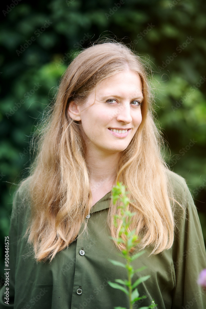 portrait of young blond woman standing outdoors in nature and smiles