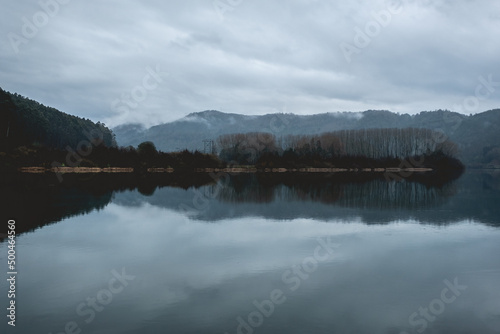 Beautiful lake in the mountains with green forest, mist, reflections in the water and cloudy sky, Valdivia, Chile