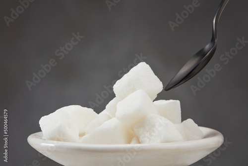 Sugar cubes in a white plate on a gray background. Shallow depth of field