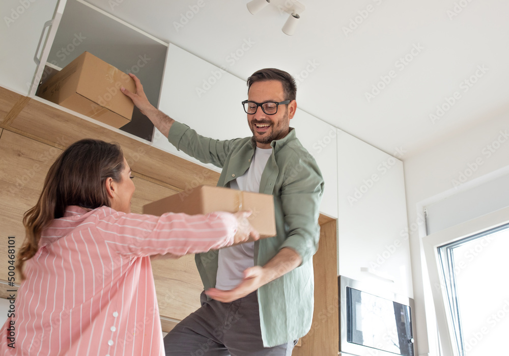 Fototapeta premium Woman helps man with heavy cardboard boxes in the kitchen.