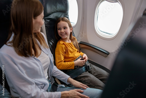 Cheerful little girl sitting next to mother in passenger airplane