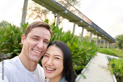 Couple laughing together while taking a selfie in a park during sunset