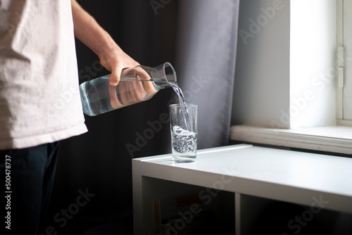 person holds a bottle and pour water in the glass