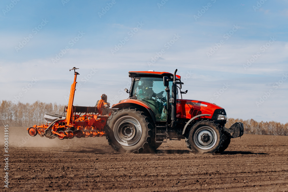 Spring sowing season. Farmer with a tractor sows corn seeds on his field. Planting corn with trailed planter. Farming seeding. The concept of agriculture and agricultural machinery.
