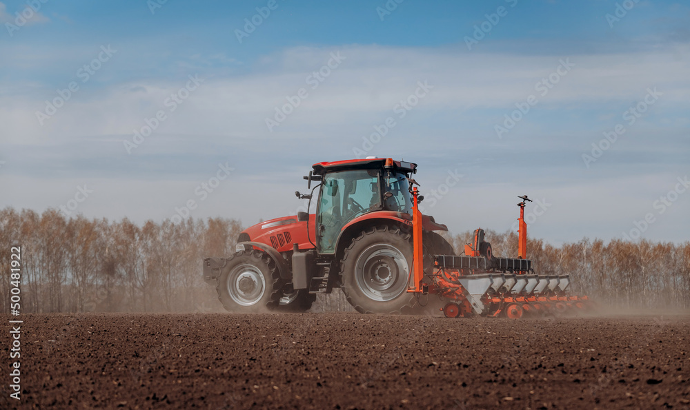 Obraz premium Spring sowing season. Farmer with a tractor sows corn seeds on his field. Planting corn with trailed planter. Farming seeding. The concept of agriculture and agricultural machinery.